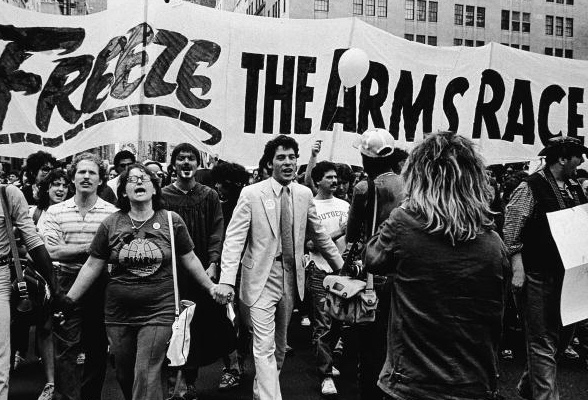Marchers walk arm in arm beneath a “Freeze the Arms Race” banner