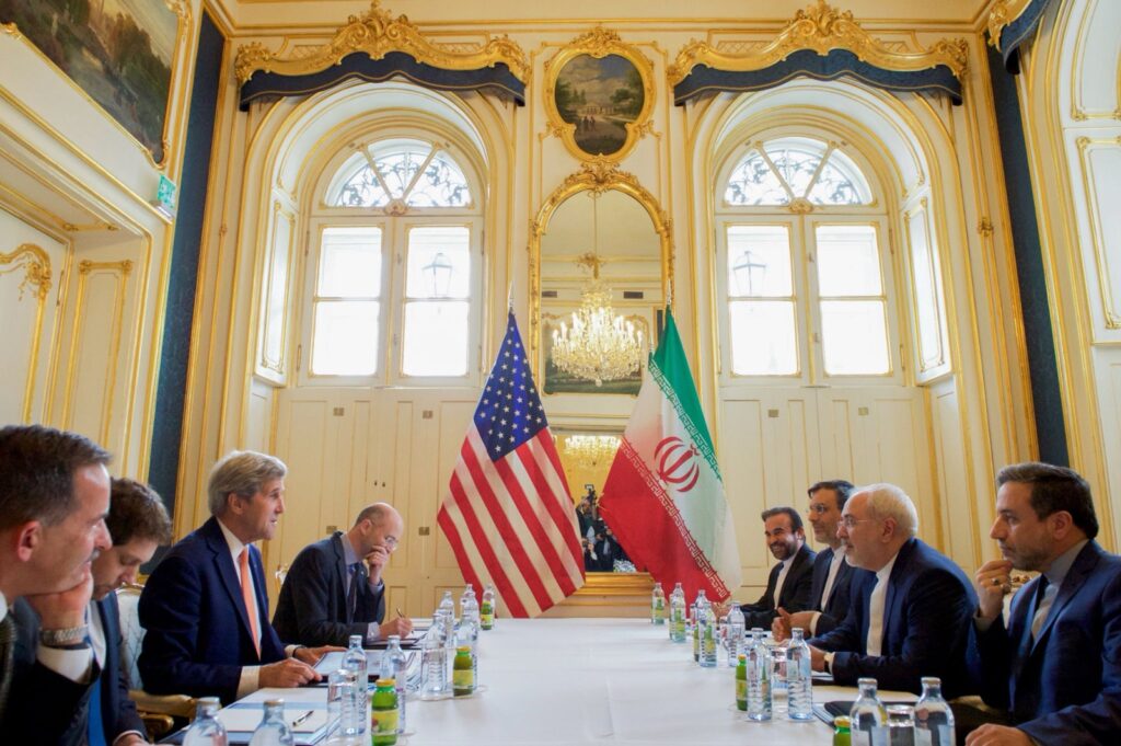 US and Iranian delegations meet across a long table beneath American and Iranian flags
