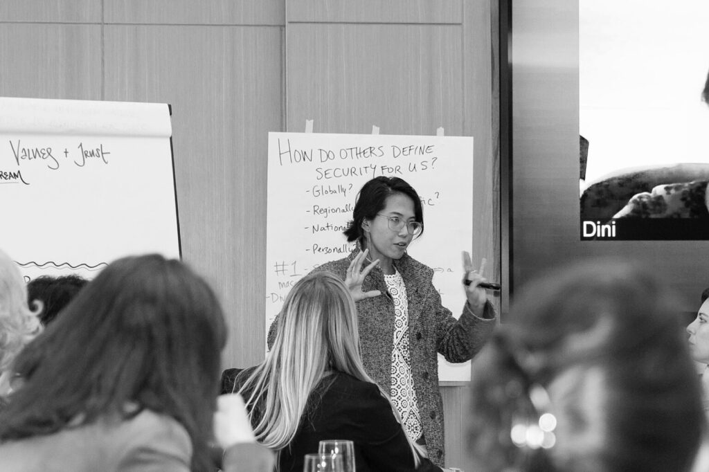 A speaker leads a session in front of a flip chart asking “How do others define security for us?”